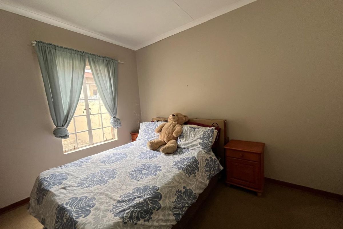 A standard bedroom featuring carpeted flooring, a window with security bars, and neutral wall tones, offering a functional space for rest.
