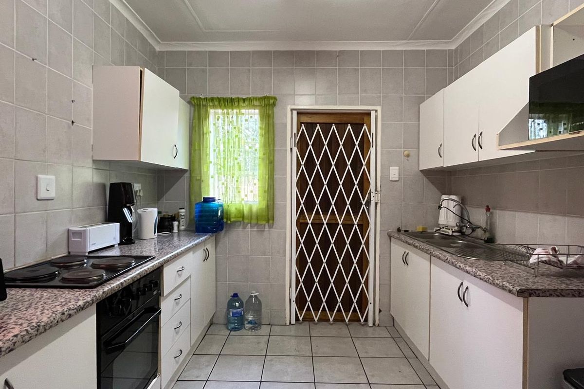 A functional galley-style kitchen featuring built-in cabinetry, laminate countertops, an electric hob, oven, and a security gate leading to the exterior.