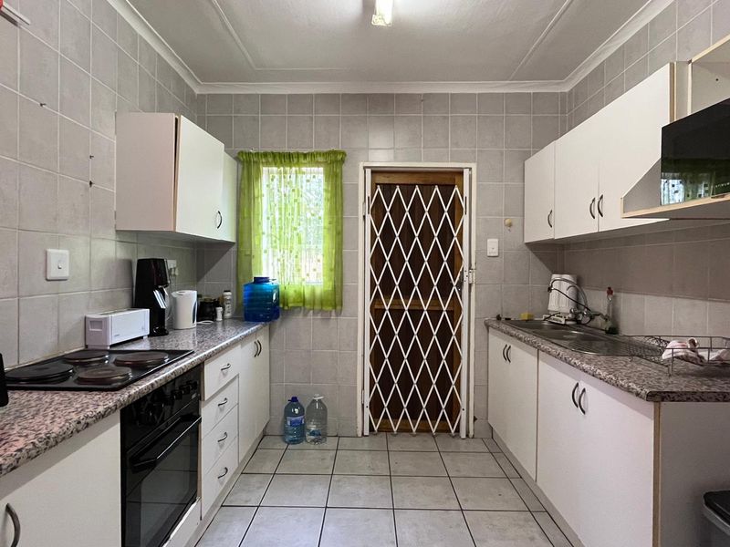 A functional galley-style kitchen featuring built-in cabinetry, laminate countertops, an electric hob, oven, and a security gate leading to the exterior.