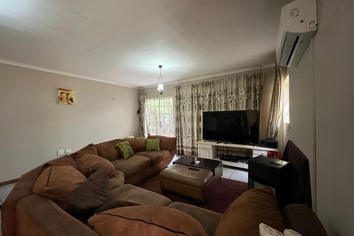 A comfortable living room featuring tiled flooring, a wall-mounted air conditioning unit, and a window with security bars.