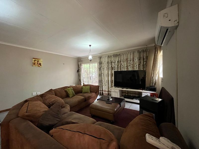 A comfortable living room featuring tiled flooring, a wall-mounted air conditioning unit, and a window with security bars.