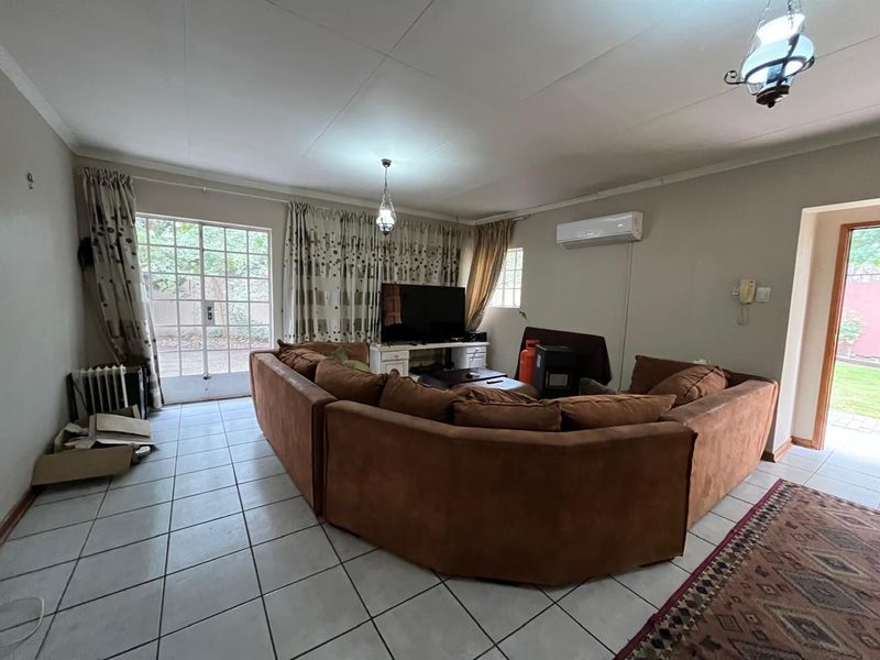 A spacious living room featuring tiled flooring, a wall-mounted air conditioning unit, and direct access to the outdoor area through a glass door.