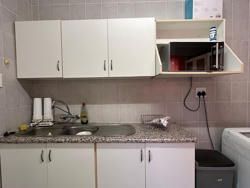 A functional laundry area featuring built-in white cabinetry, a stainless steel sink, tiled backsplash, and dedicated space for a microwave and washing machine.