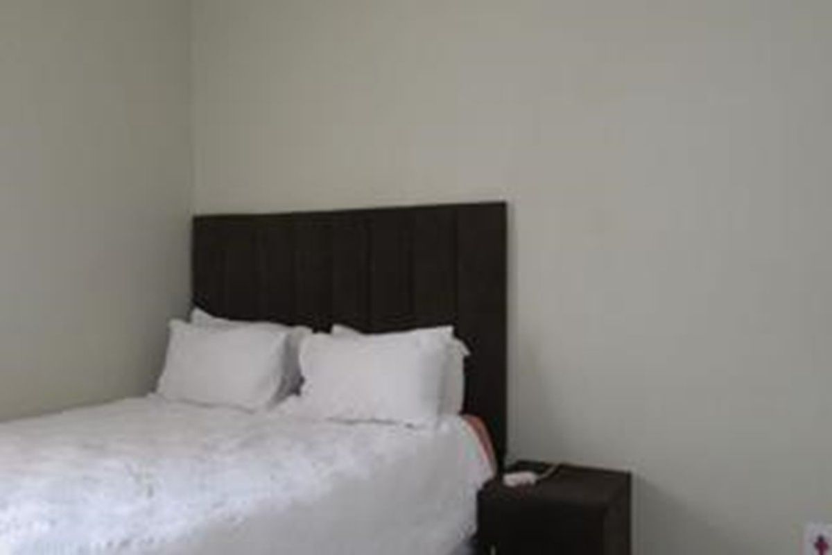 A simple bedroom featuring neutral walls and a dark upholstered headboard, providing a clean and functional sleeping space.