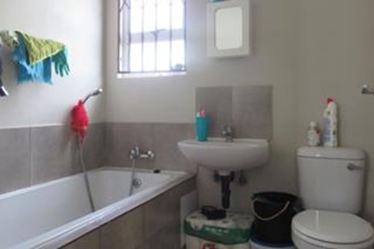 A functional bathroom featuring a bathtub with shower mixer, wall-mounted basin, and toilet, finished with neutral wall tiles.
