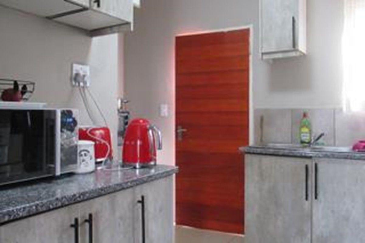 A functional kitchen featuring grey cabinetry, granite-style countertops, and a solid wood door, providing a practical workspace for daily meal preparation.