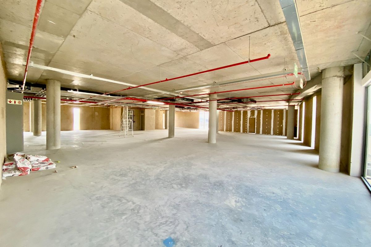 A large, open-plan commercial space in shell condition, featuring exposed concrete ceilings, structural columns, and visible fire suppression infrastructure.
