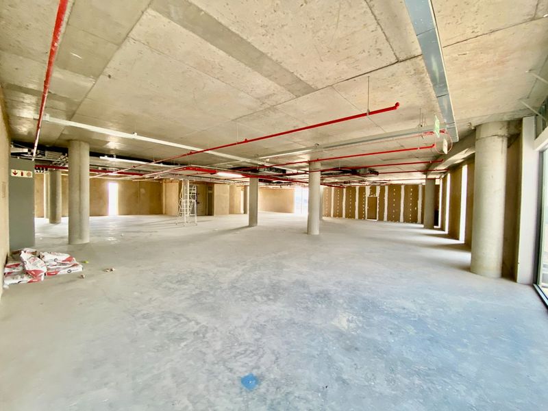 A large, open-plan commercial space in shell condition, featuring exposed concrete ceilings, structural columns, and visible fire suppression infrastructure.