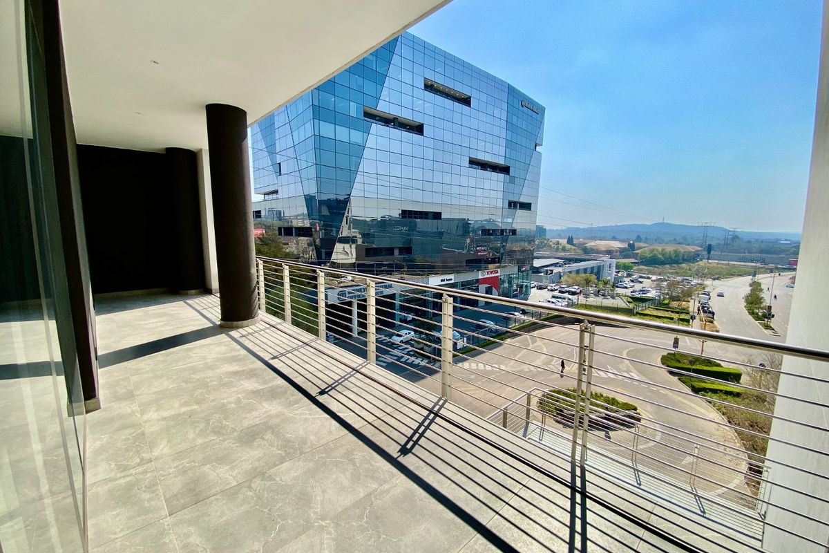 A modern, covered balcony featuring tiled flooring and a stainless steel balustrade, offering an elevated view of the surrounding commercial area.