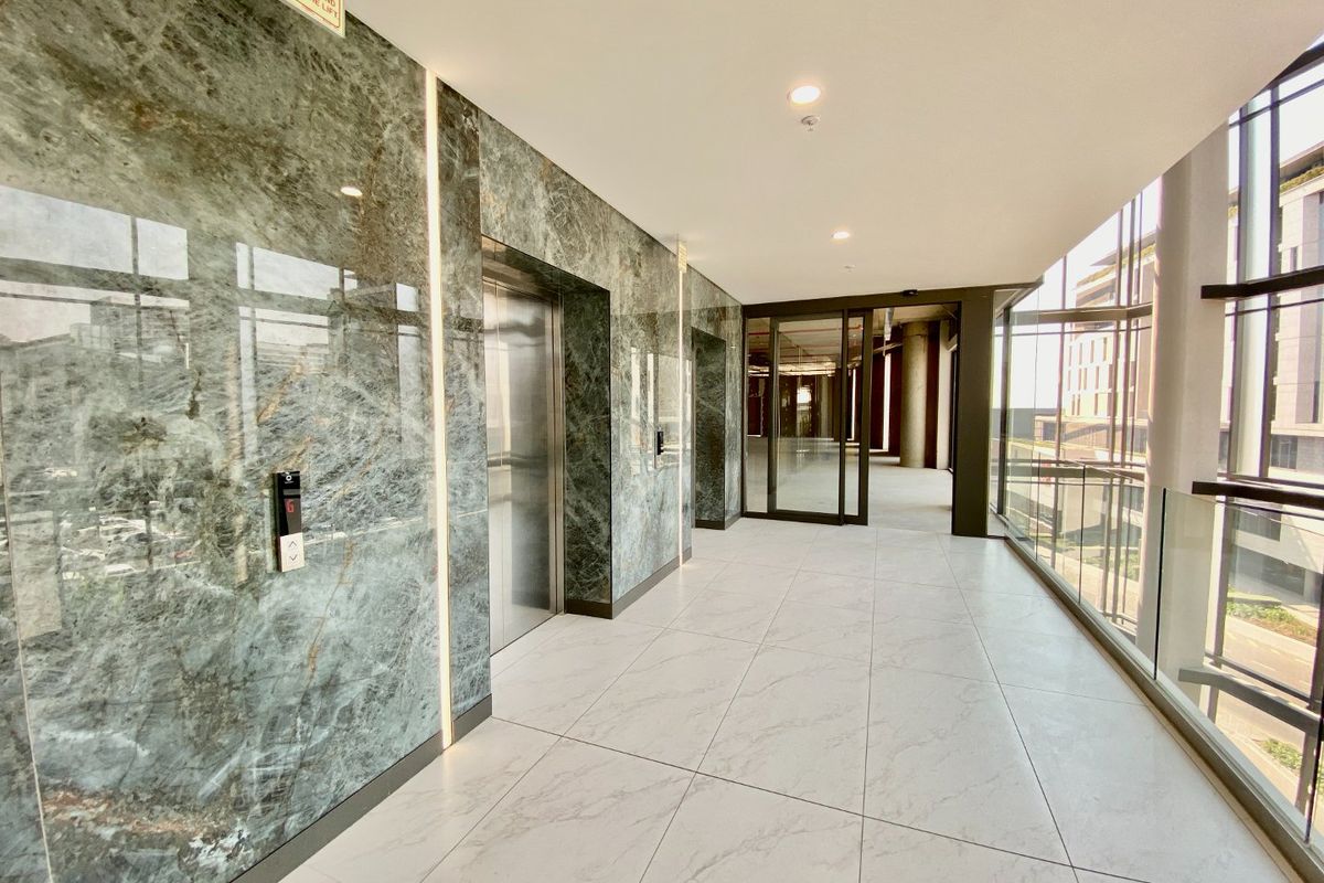 Modern commercial hallway featuring premium marble wall cladding, large format floor tiles, stainless steel elevator access, and expansive floor-to-ceiling glass windows.