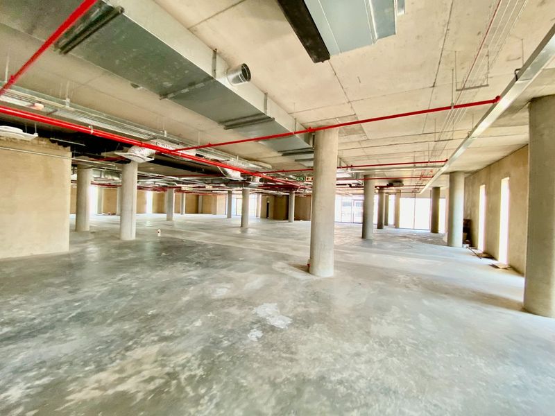 A large, open-plan commercial shell space featuring exposed concrete ceilings, industrial ducting, fire sprinkler systems, and polished concrete flooring throughout.