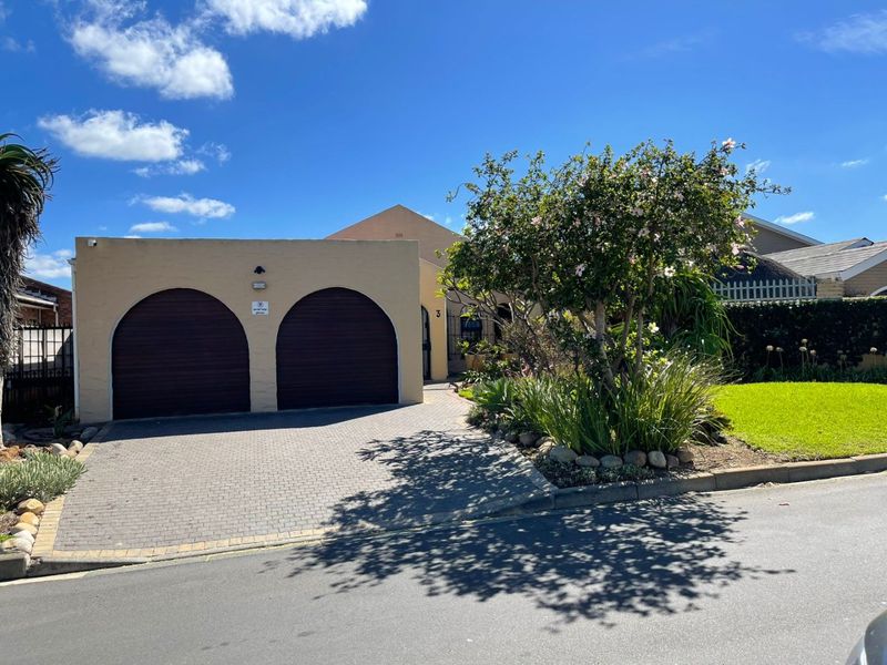 Front elevation of a residential property featuring a double garage with arched doors, a paved driveway, and a well-maintained front garden.