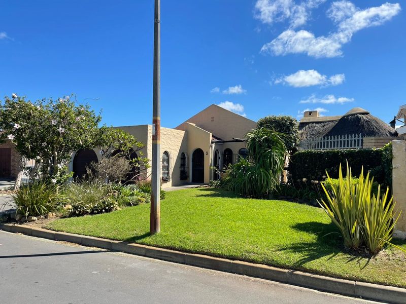 Front elevation of a single-story house featuring a landscaped front garden, arched windows with security bars, and a paved driveway.