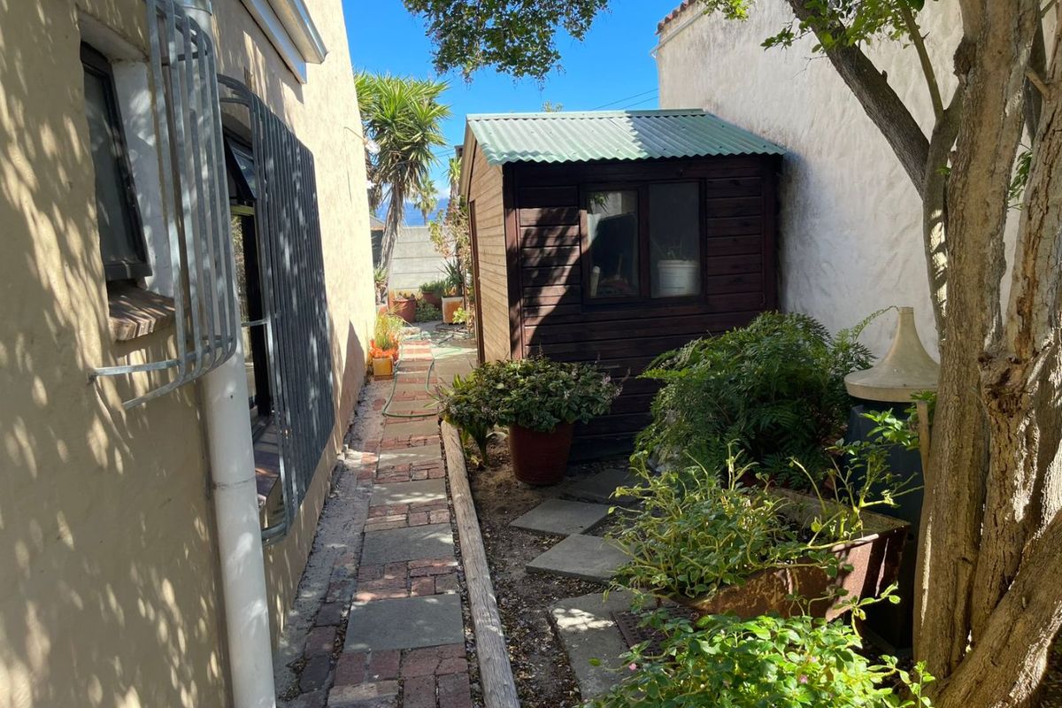 A narrow rear garden area featuring a timber storage shed, brick paved pathway, and established greenery along the side of the property.