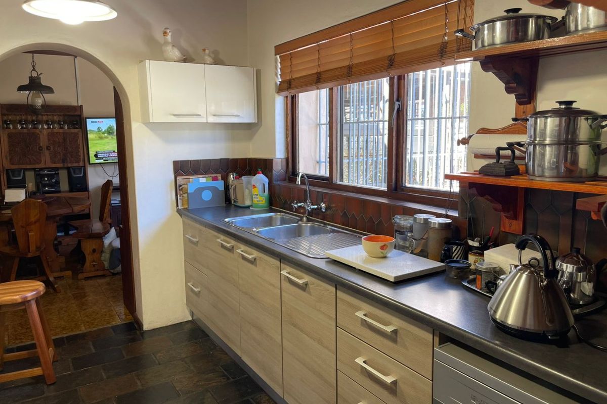 A functional kitchen featuring laminate cabinetry, a double bowl stainless steel sink, slate flooring, and a tiled splashback with views through timber-blinded windows.