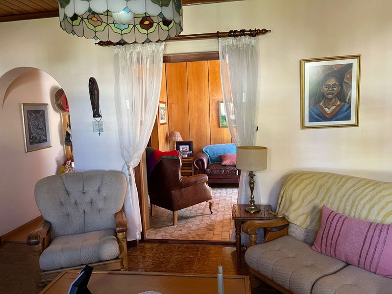 A cozy living room featuring a timber ceiling, tiled flooring, and an arched entryway leading to an adjacent room with wood paneling.