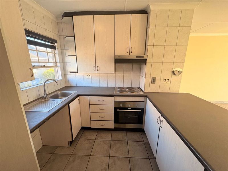 A functional kitchen featuring laminate cabinetry, built-in oven, electric hob, extractor fan, and tiled finishes throughout.