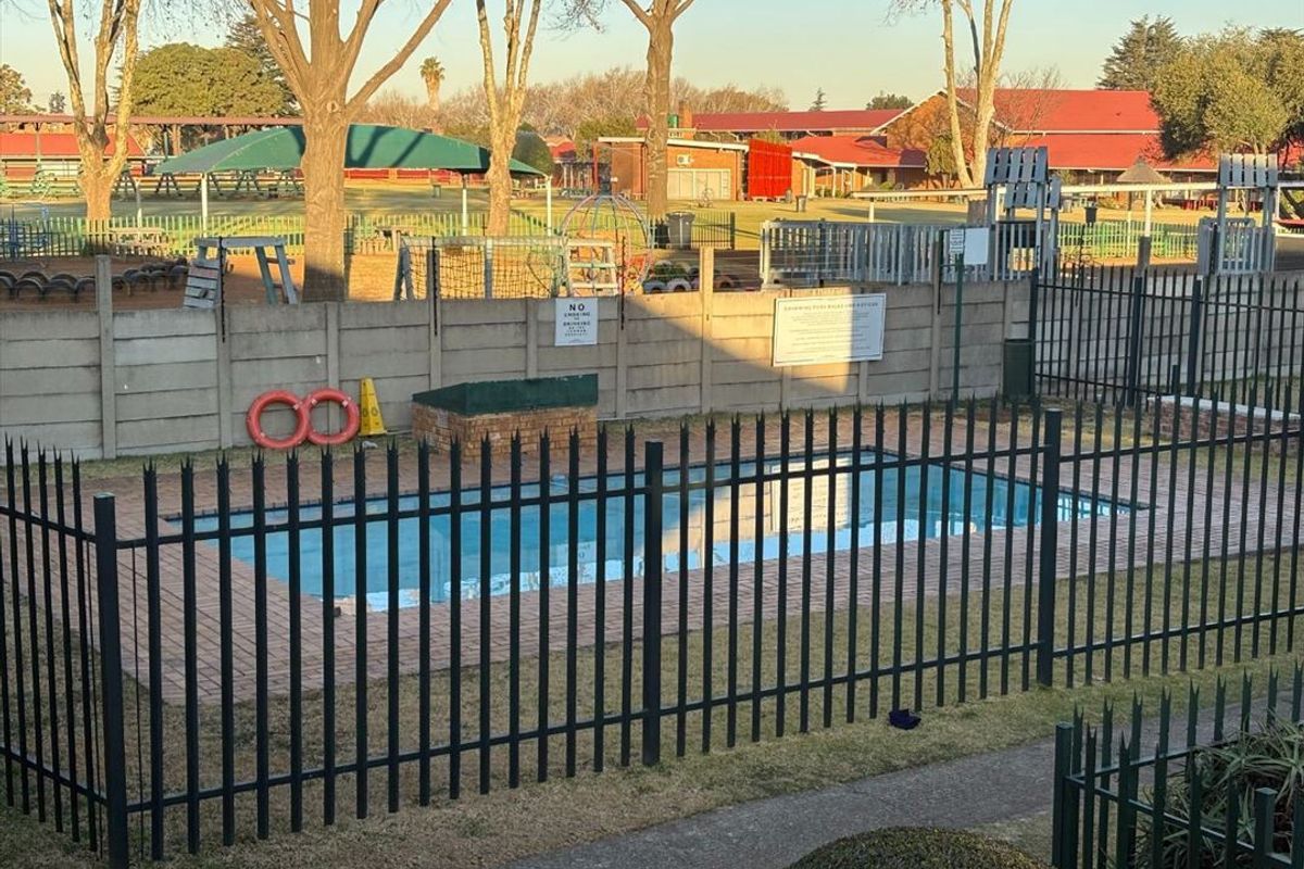 A communal swimming pool area featuring brick paving, secure metal fencing, and a precast concrete boundary wall.