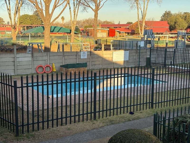 A communal swimming pool area featuring brick paving, secure metal fencing, and a precast concrete boundary wall.