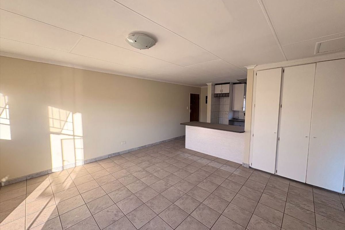 An open-plan living area featuring tiled flooring, built-in storage cupboards, and a breakfast bar connecting to the kitchen space.