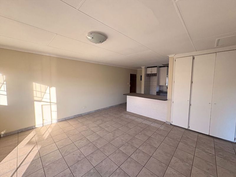 An open-plan living area featuring tiled flooring, built-in storage cupboards, and a breakfast bar connecting to the kitchen space.
