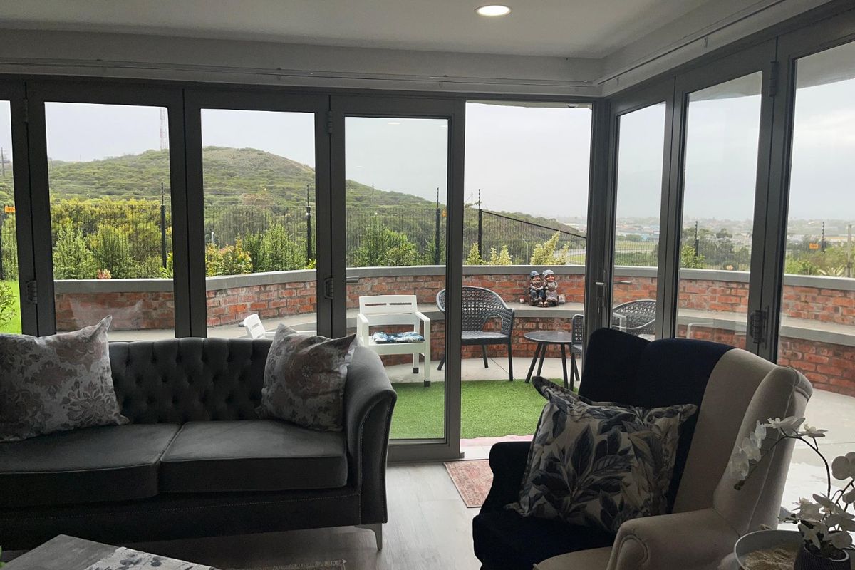 Bright living room featuring expansive bi-fold glass doors that open onto a private balcony with scenic views and a brick boundary wall.
