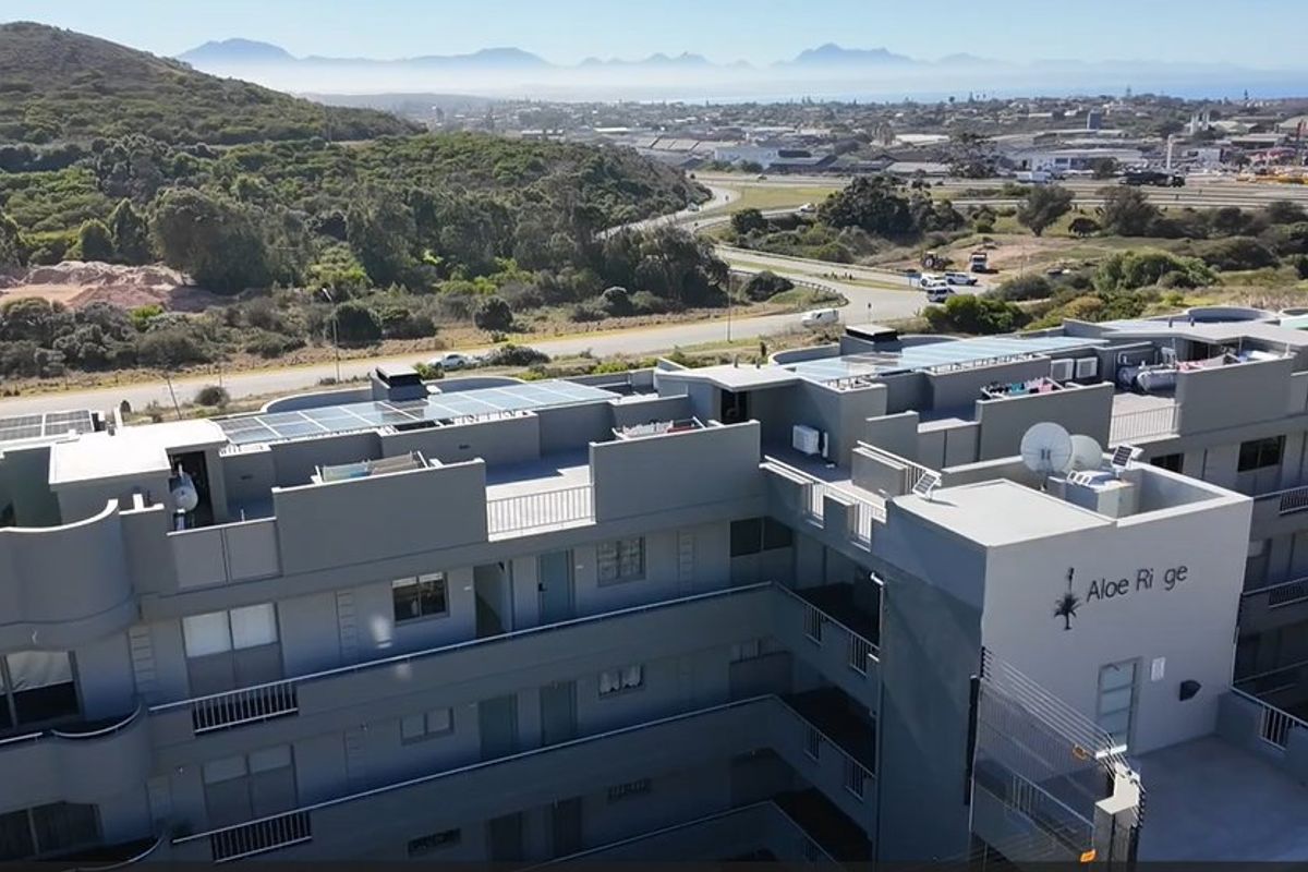 Aerial view of the Aloe Ridge apartment complex, showcasing the building exterior, rooftop solar installations, and surrounding landscape.