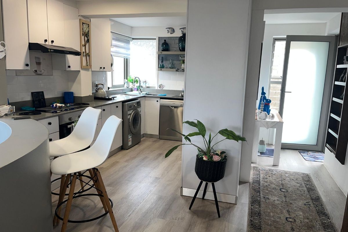 A functional kitchen featuring white cabinetry, integrated appliances, a tiled backsplash, and wood-look laminate flooring, seamlessly connected to the living area.