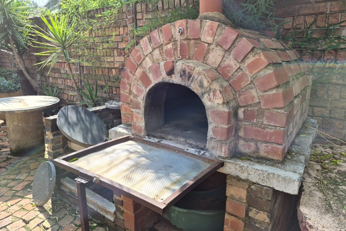 A rustic outdoor brick pizza oven situated in a paved garden area with a brick boundary wall.