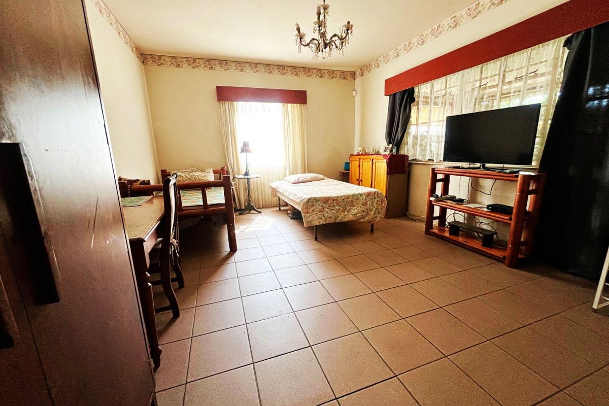 A spacious bedroom featuring ceramic floor tiles, a decorative chandelier, and a floral wallpaper border, offering a functional layout with natural light.