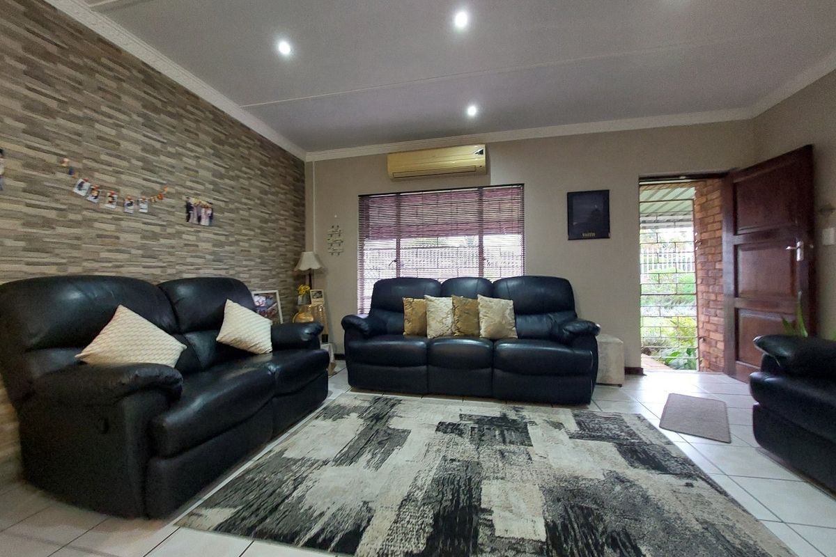 A living room featuring tiled flooring, a stone-cladding feature wall, recessed downlights, and a wall-mounted split-system air conditioner.