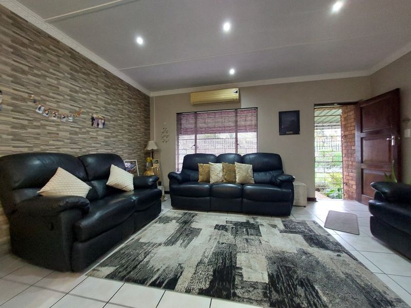 A living room featuring tiled flooring, a stone-cladding feature wall, recessed downlights, and a wall-mounted split-system air conditioner.