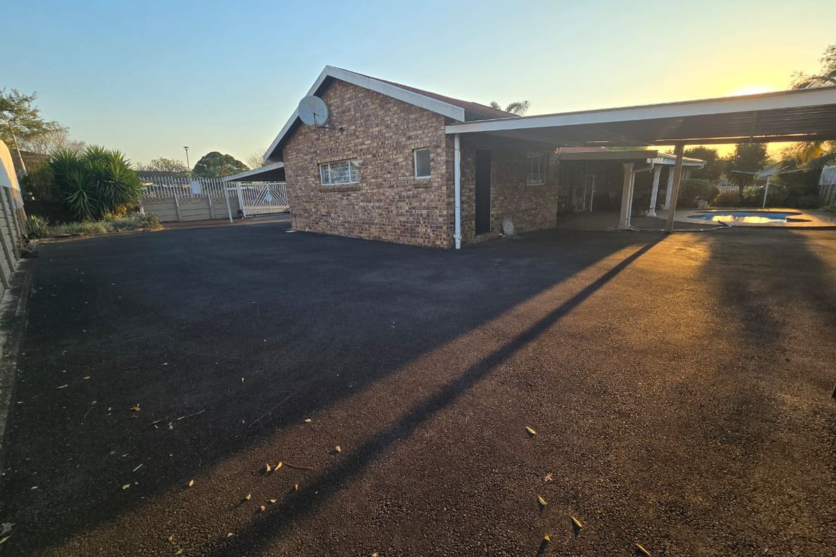 Rear exterior view of the property featuring a brick facade, expansive asphalt driveway, covered carport area, and a swimming pool.