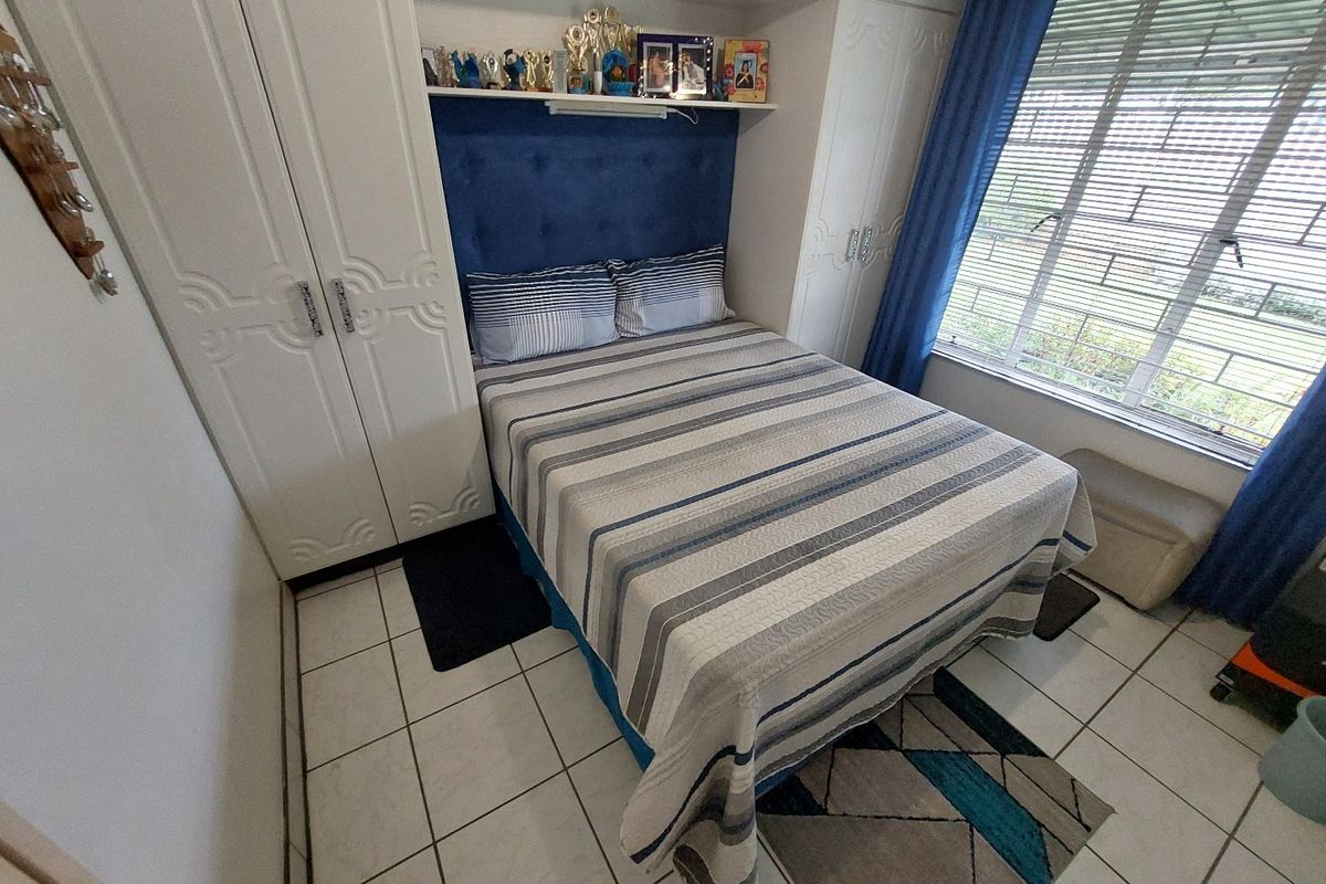 A compact bedroom featuring built-in cupboards, tiled flooring, and a window with venetian blinds, offering a functional and well-organized living space.