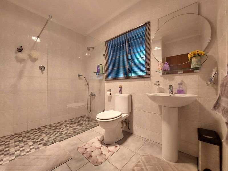 A functional bathroom featuring a walk-in shower with a glass screen, pedestal basin, and tiled finishes throughout.