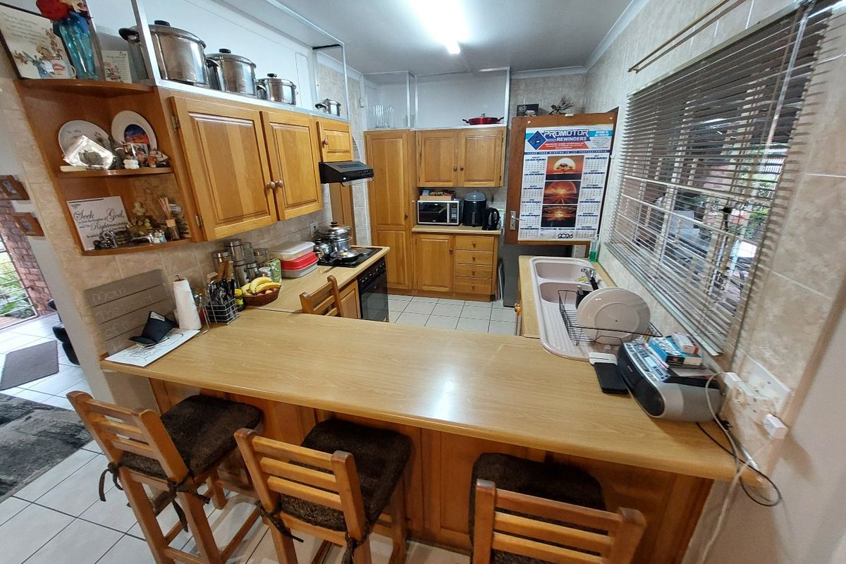 A functional kitchen featuring wooden cabinetry, a breakfast bar, double basin sink, and built-in cooking appliances with tiled flooring throughout.