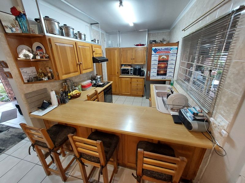 A functional kitchen featuring wooden cabinetry, a breakfast bar, double basin sink, and built-in cooking appliances with tiled flooring throughout.