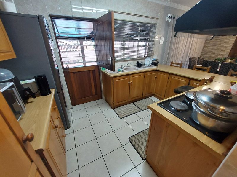 A functional kitchen featuring wooden cabinetry, tiled flooring, a double sink, and an integrated electric hob with an overhead extractor fan.