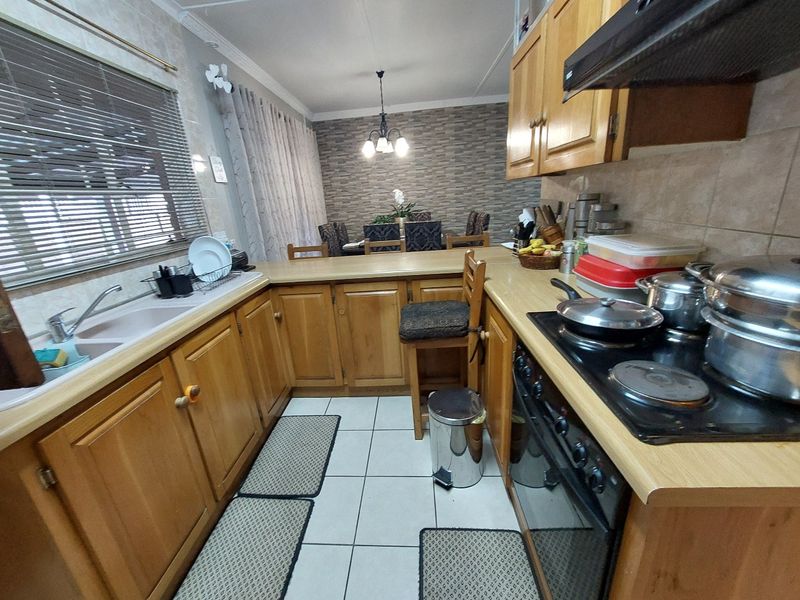 A functional kitchen featuring wooden cabinetry, laminate countertops, built-in oven, electric hob, and tiled flooring, with an adjacent dining area.