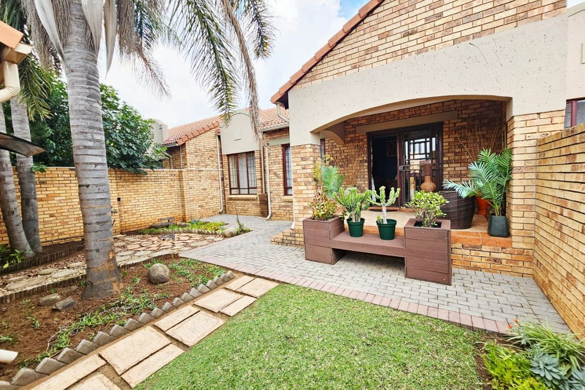 A well-maintained rear exterior featuring a face brick townhouse facade, a covered patio, paved walkways, and a landscaped garden area.