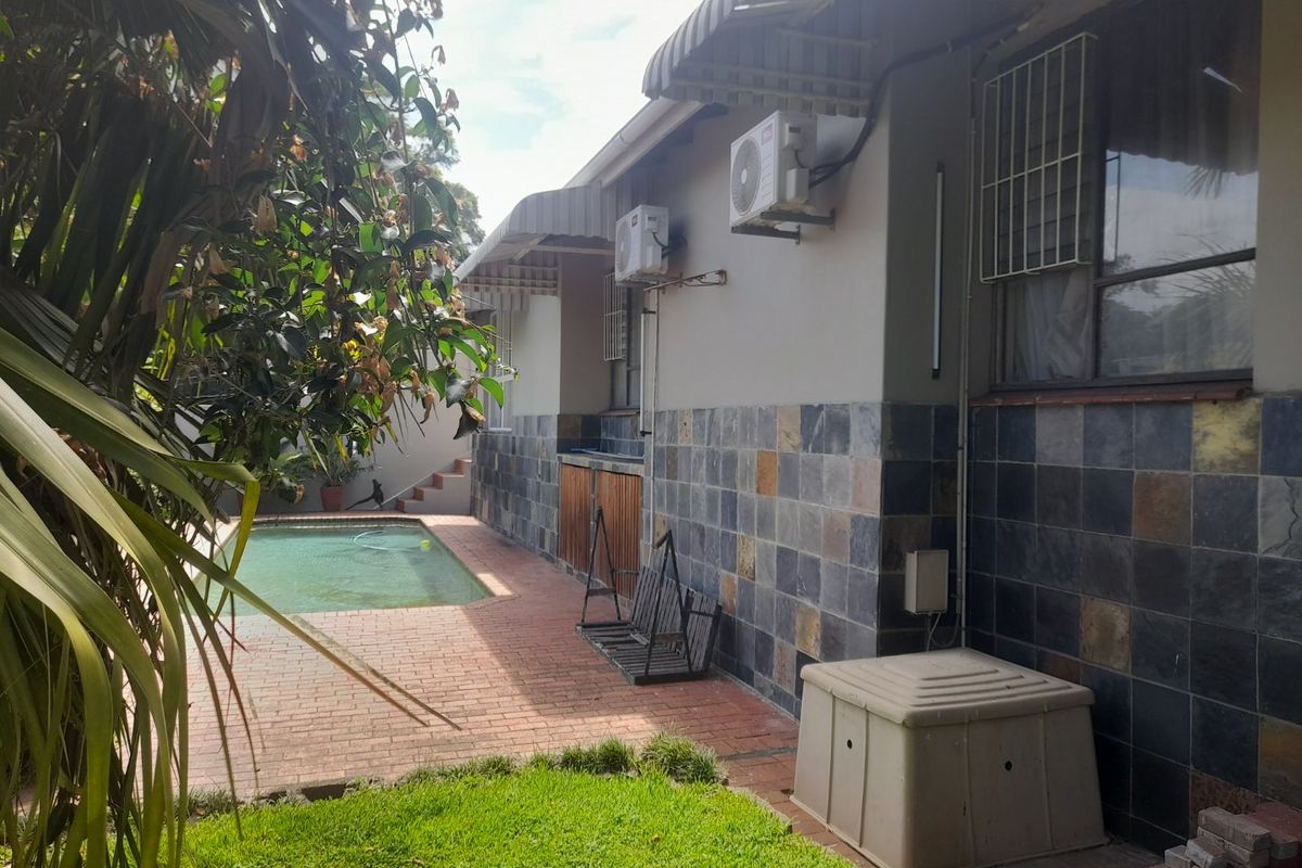 Rear exterior view featuring a swimming pool, brick paved patio area, and slate-clad wall finishes with mounted air conditioning units.