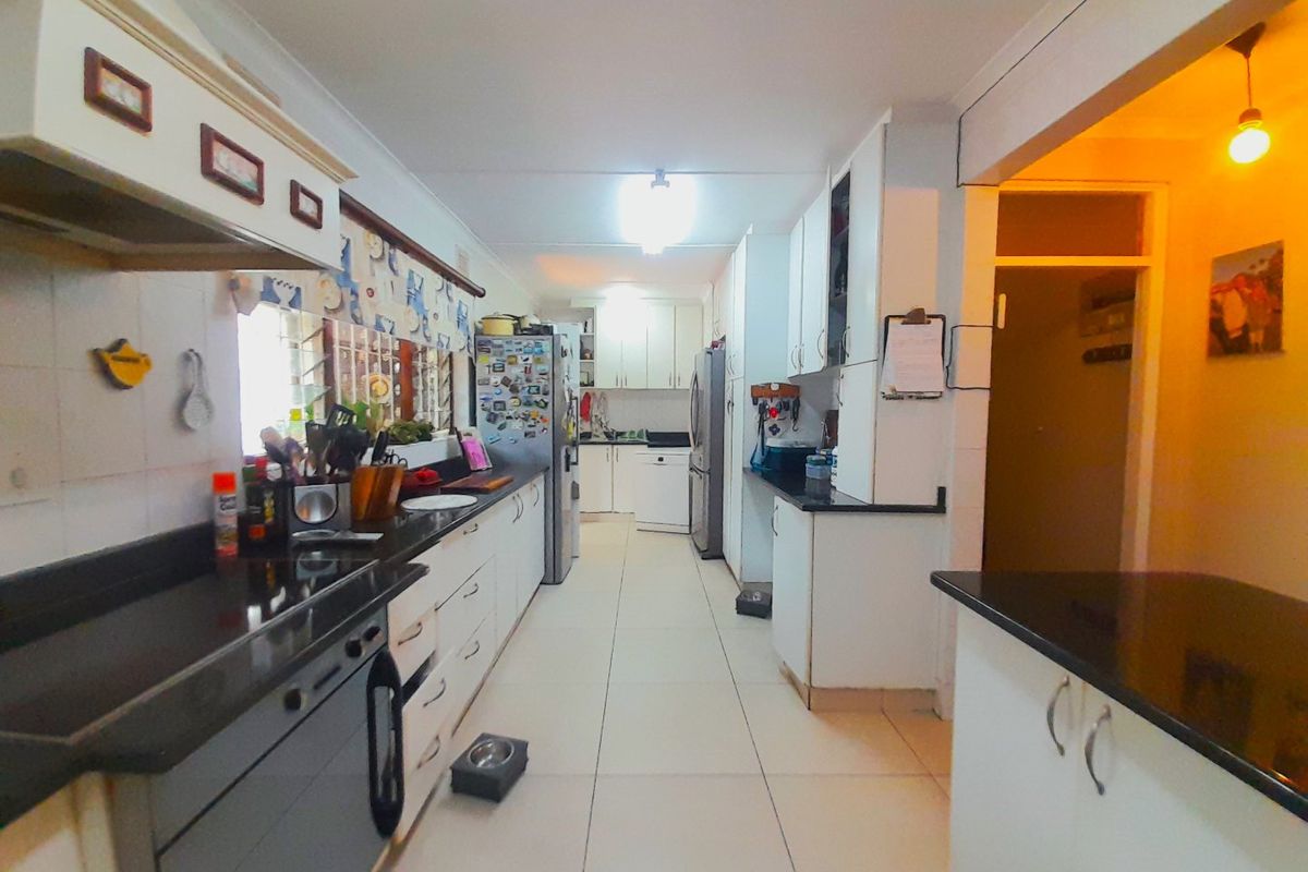 A functional kitchen featuring white cabinetry, dark granite countertops, tiled flooring, and an integrated extractor fan, offering ample storage and workspace.