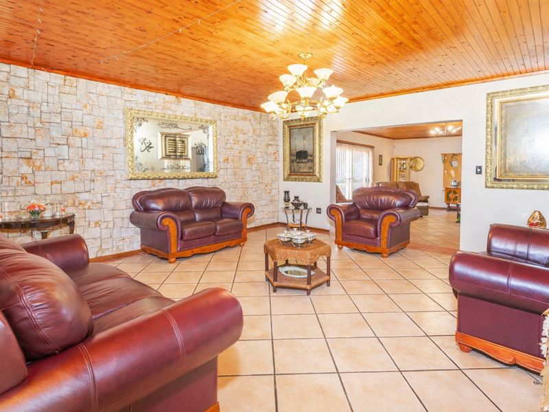 Spacious living room featuring a distinctive stone accent wall, warm timber ceiling, and neutral ceramic floor tiles, offering a classic and inviting atmosphere.