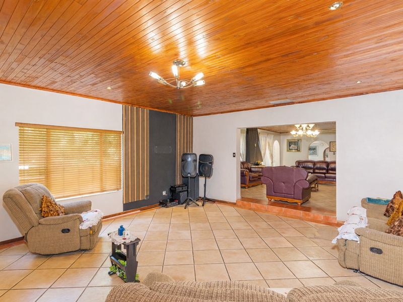 Spacious living area featuring a warm wooden tongue and groove ceiling, ceramic tiled flooring, and a raised transition leading to an adjacent lounge space.