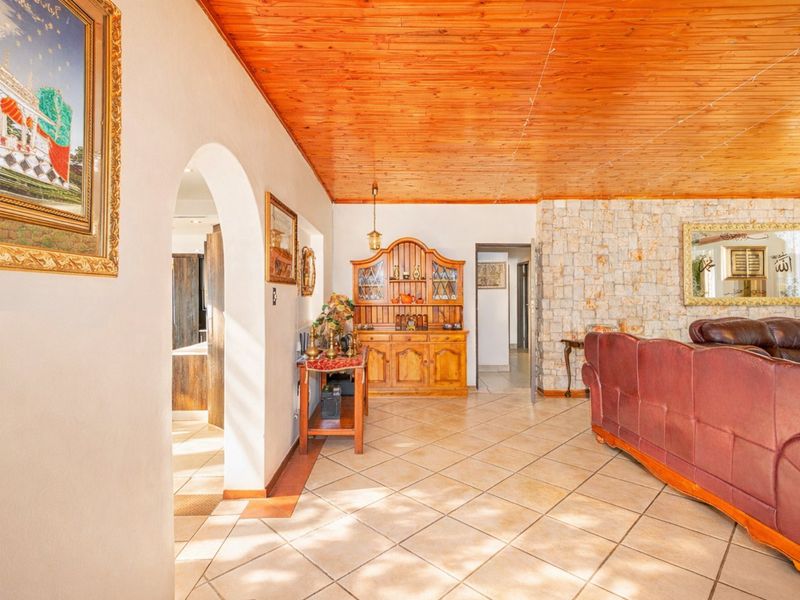 Spacious living area featuring a warm timber-clad ceiling, stone feature wall, and neutral ceramic floor tiles with an inviting arched entryway.