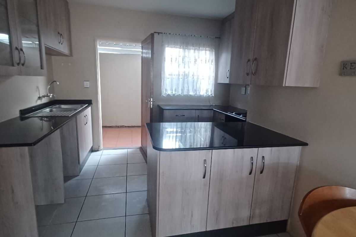 A functional kitchen featuring light wood-grain cabinetry, dark granite countertops, and tiled flooring, with an adjacent utility area visible through the doorway.