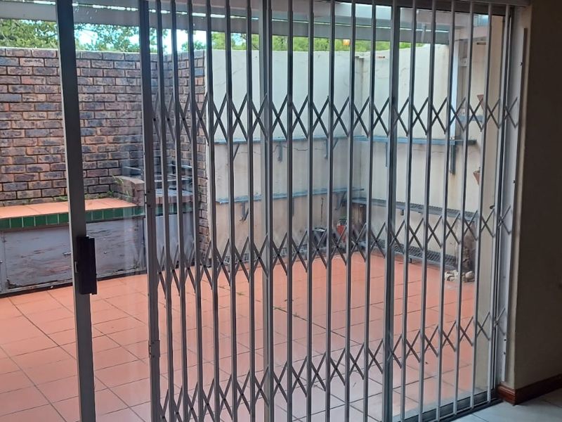 Covered patio area featuring a built-in braai, tiled flooring, and a utility sink, secured by a metal sliding gate.