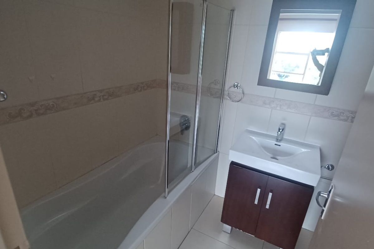 A functional bathroom featuring a bathtub with a glass screen, a vanity cabinet with a basin, and neutral wall and floor tiling.