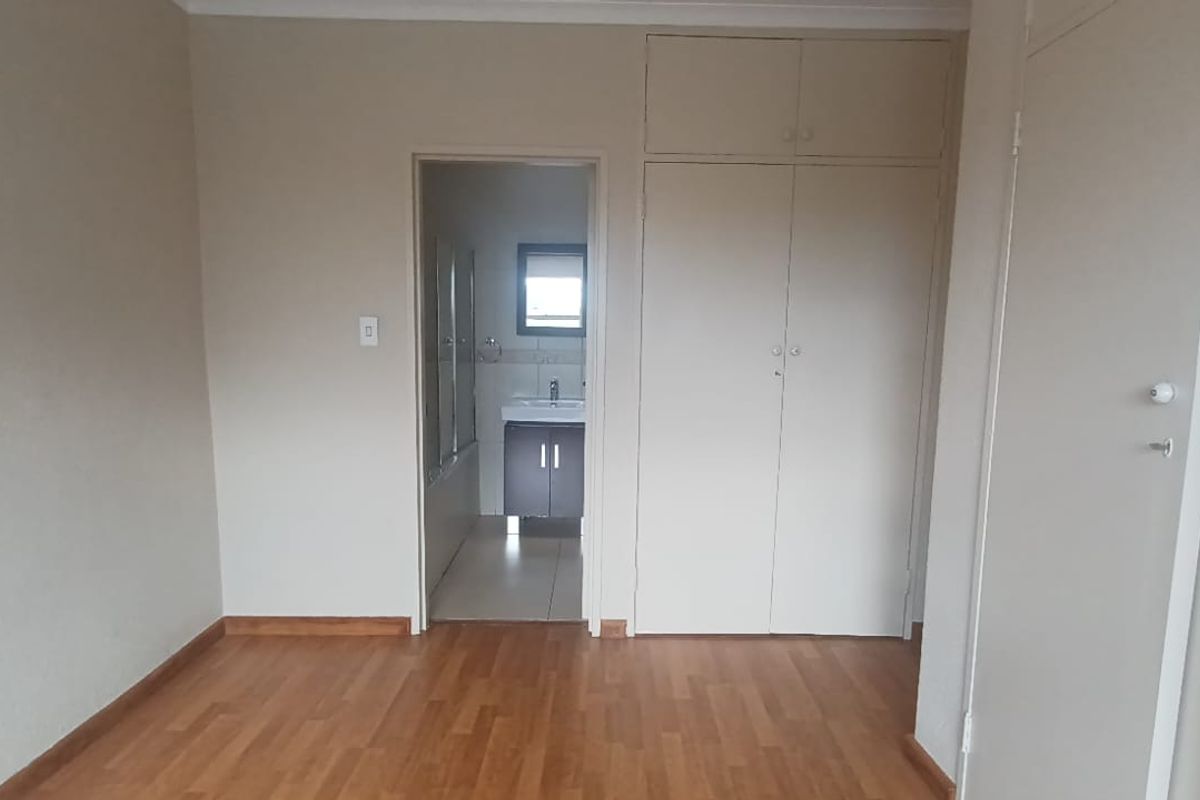 A spacious, empty bedroom featuring laminate flooring, built-in cupboards with overhead storage, and direct access to an en-suite bathroom.