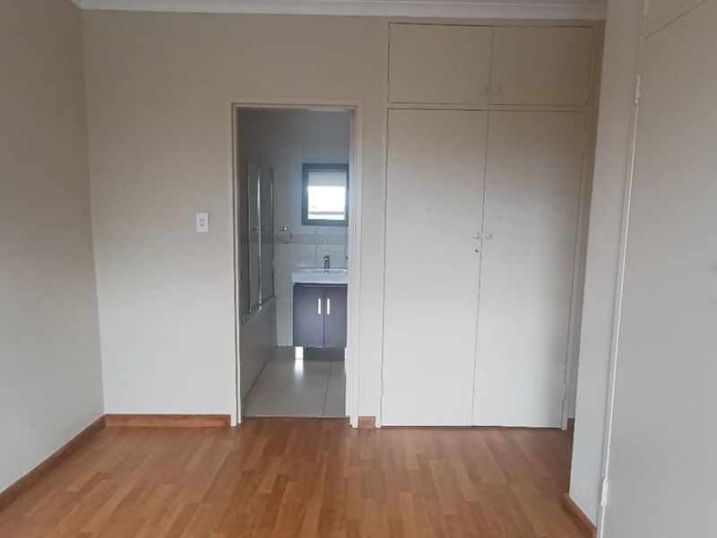 A spacious, empty bedroom featuring laminate flooring, built-in cupboards with overhead storage, and direct access to an en-suite bathroom.